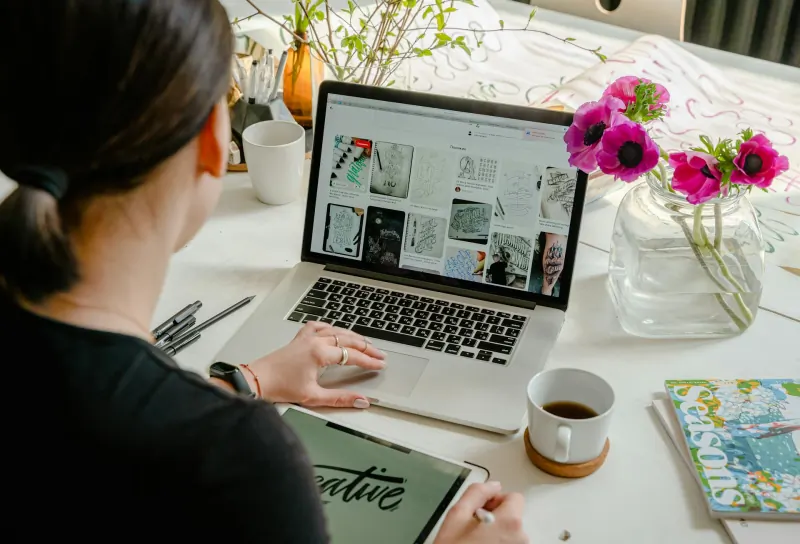 A designer reviewing brand reference boards on a laptop with sketches on a tablet